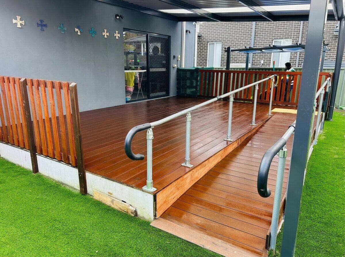 Before — VD Painting crew member applying stain to a weathered timber deck under a patio in NSW